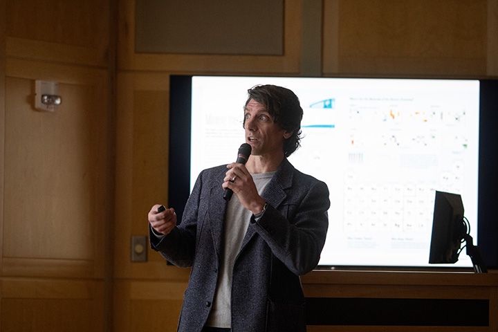 Graphic Designer Oliver Uberti holds a microphone and speaks in front of a crowd.