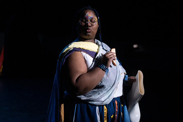 A student actor stands on stage with the spotlight pointing at her.