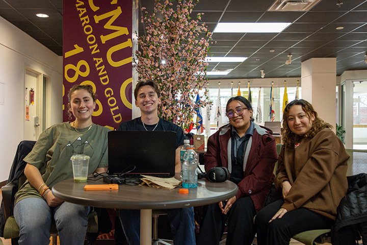 Four students sit at a small round table smiling for the camera.