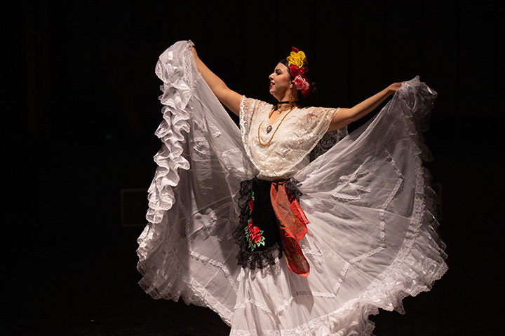 A female latin dancer poses in front of a black background.
