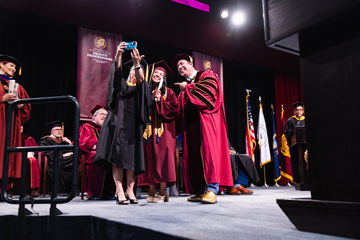 A group of people in graduation gowns take a selfie.