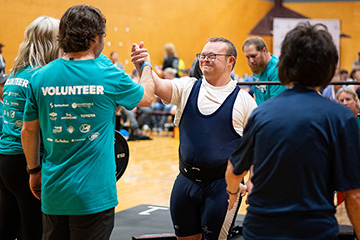 A Special Olympics athlete in a powerlifting uniform high fives a volunteer in a blue shirt.