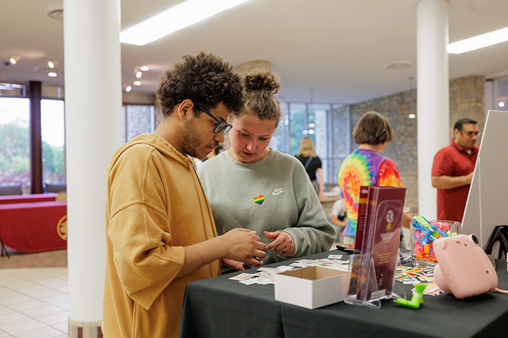 Two people stand at a table looking at small instant photos spread out across the table.