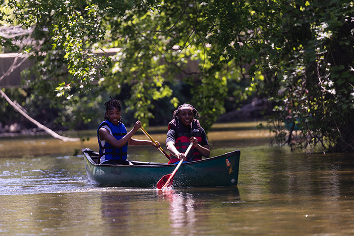 Two people paddle down a river in a canoe.