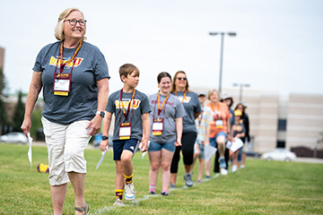 A group of people consisting of grandparents and their grandchildren march in a line on a football field.