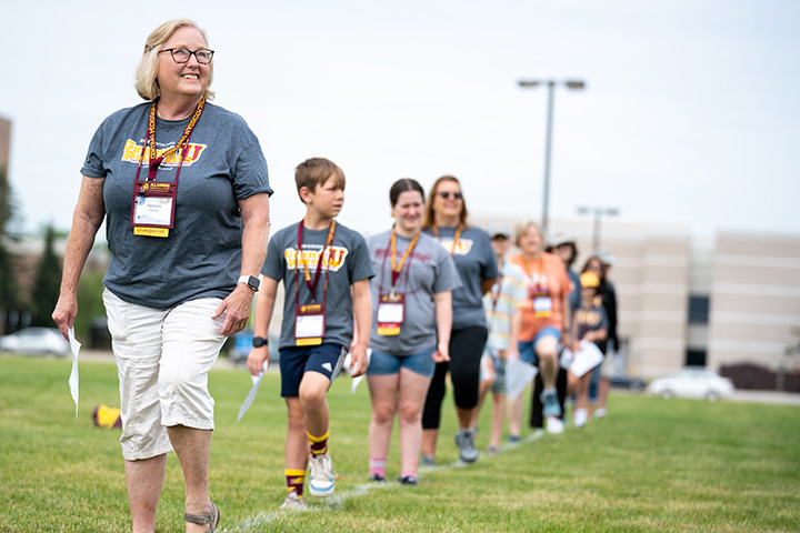 A group of people consisting of grandparents and their grandchildren march in a line on a football field.