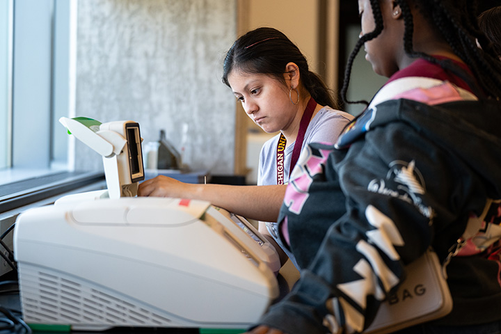 Two high school students stand next to a computer.