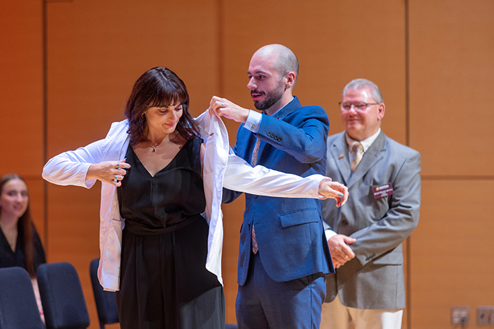 A man in a suit puts a white coat on a female student.