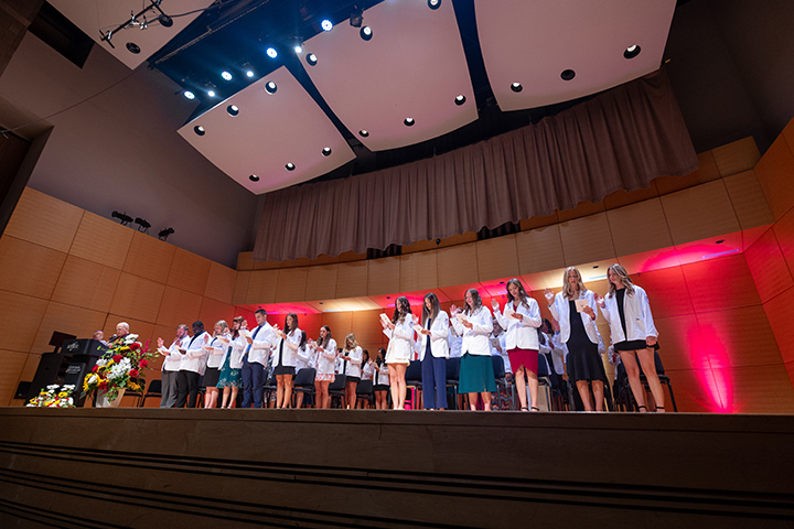 A group of students on a stage wearing white coats.