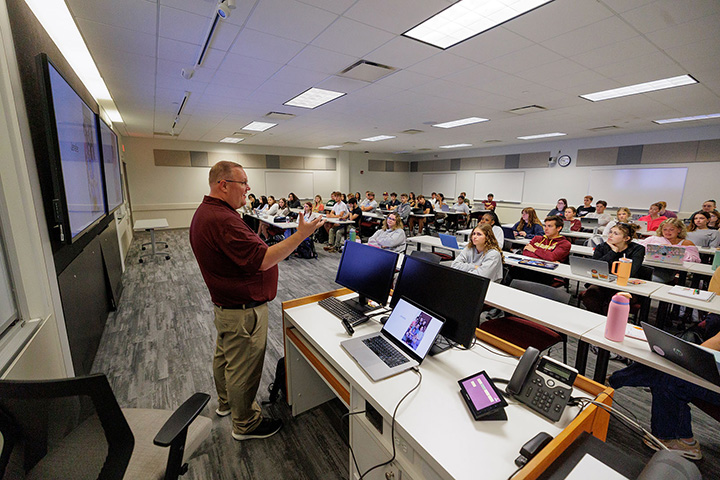 A man standing in front of a classroom with a group of students