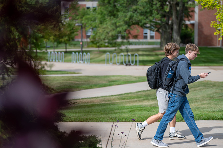 Two men wearing backpacks walking on a sidewalk.