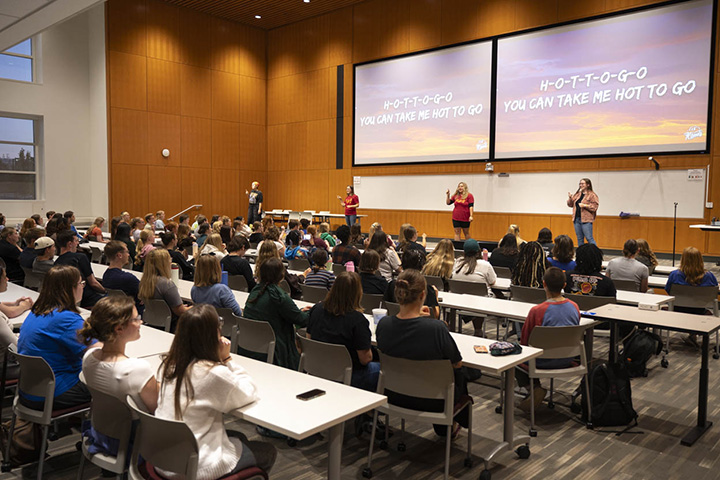 ASL interpreters stand in front of group of people in a room with a large screen