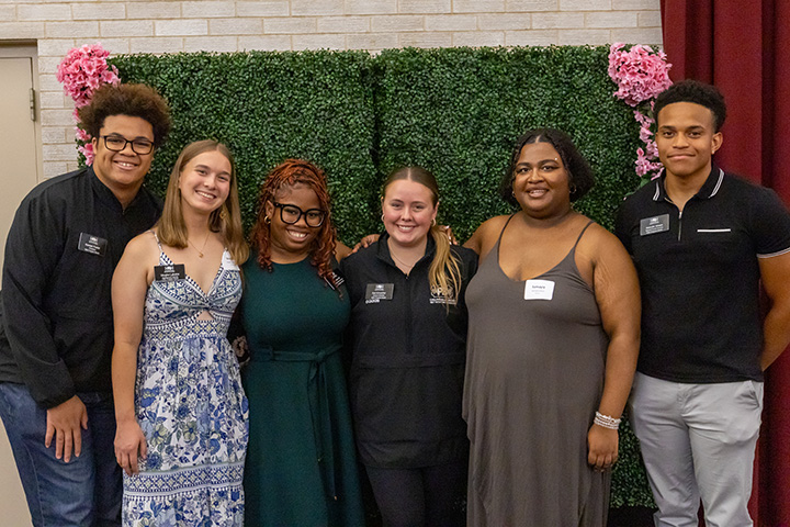 A group of students posing for a photo in front of a fake floral background.