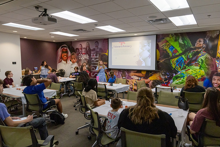 A group of parents and K-12 students sitting at tables in a room with a projector screen