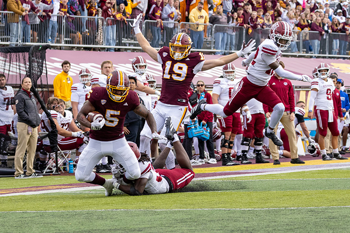 A CMU football player gets tackled as other players run behind