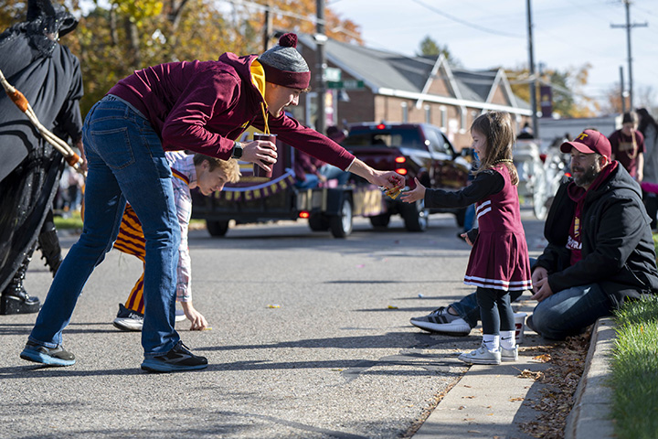 A man hands some candy to a child dressed as a cheerleader