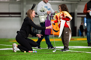 A woman and a young child dressed in halloween costumes hold a golf club