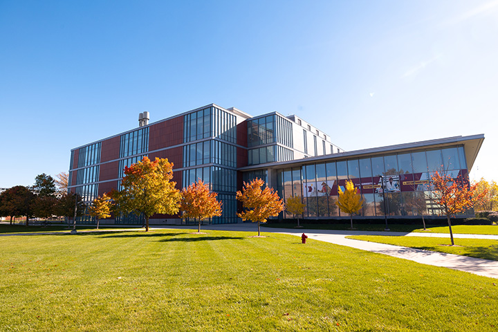A wide angle shot of the CMU Biosciences Building with colorful fall trees lining the walkway around the building