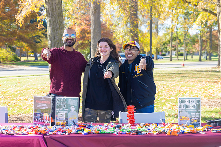 Three people pose for a group photo while smiling in front of a table full of candy