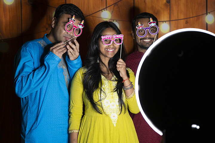 A group of people posing for a photo wearing Diwali-themed party glasses