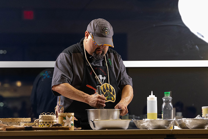 A man in a baseball hat mixing food in a bowl on a table