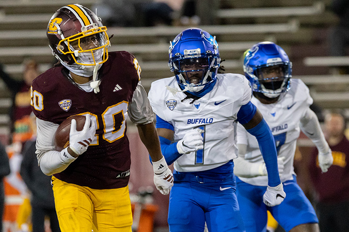 A CMU football player holding a football player gets chased by two Buffalo football players