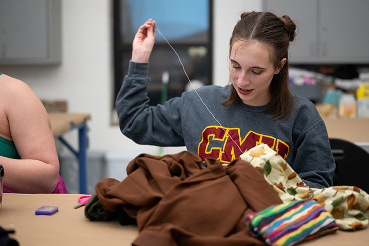A female student in a CMU sweatshirt sits at a table sewing costumes