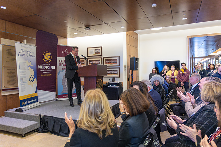President MacKinnon stands at a podium in front of a crowd