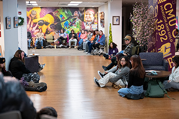 A large group of students sit along the ground and walls in a large room
