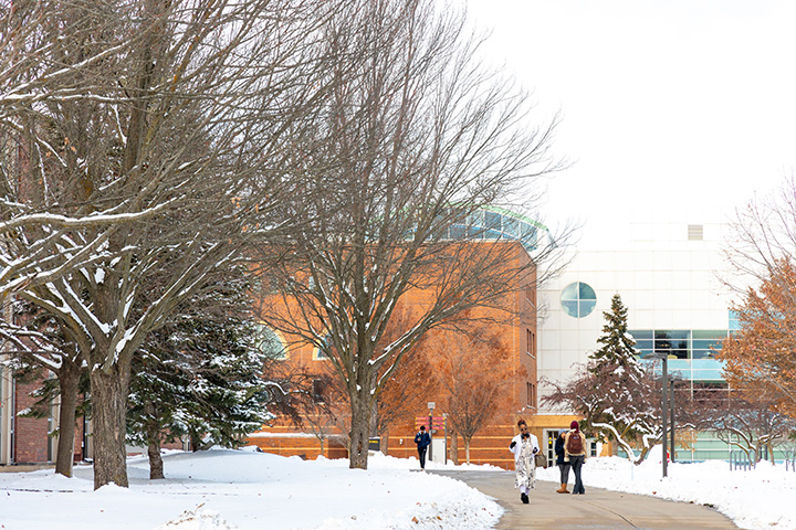 People walk down the sidewalk near the Park Library on a snowy day at CMU.