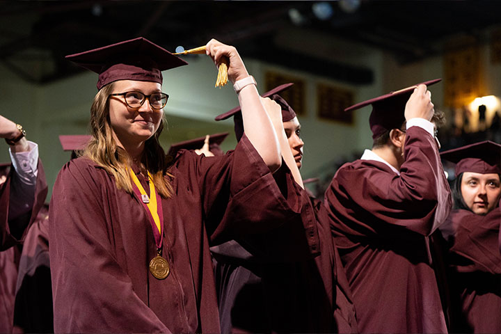 A group of people in maroon graduation gowns holding gold tassels on their cap.