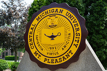 A maroon and golden sign among trees.