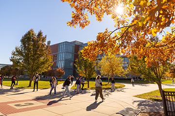 A group of students walking past colorful trees on a sidewalk in front of a building.