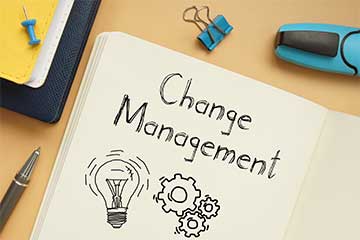 An open notebook with the words Change Management in print text with doodles of lightbulbs and gears