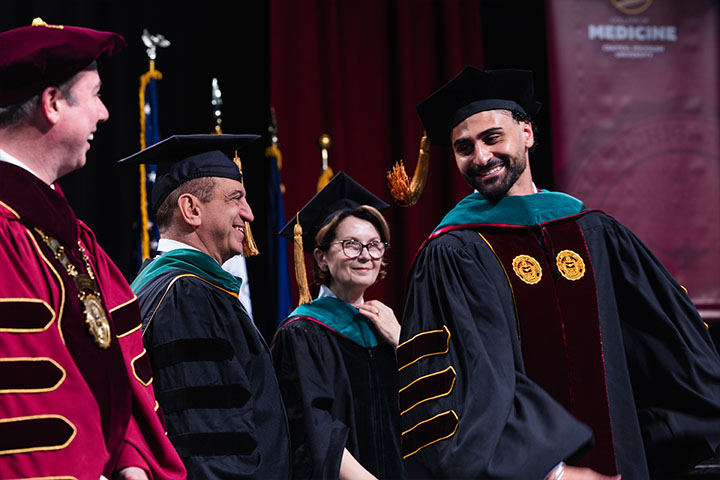 A group of people wearing graduation gowns and caps smiling.