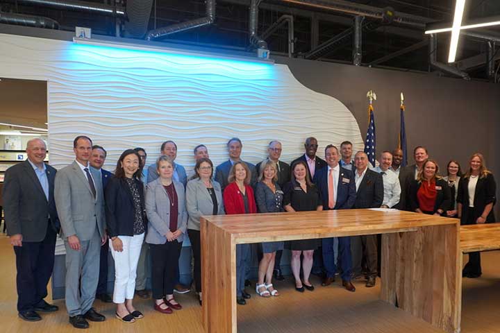 A diverse group of people in business attire stand behind a large wooden desk in a large meeting room