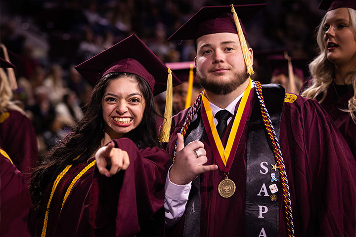 A man and woman in graduation gowns and cap and gowns.
