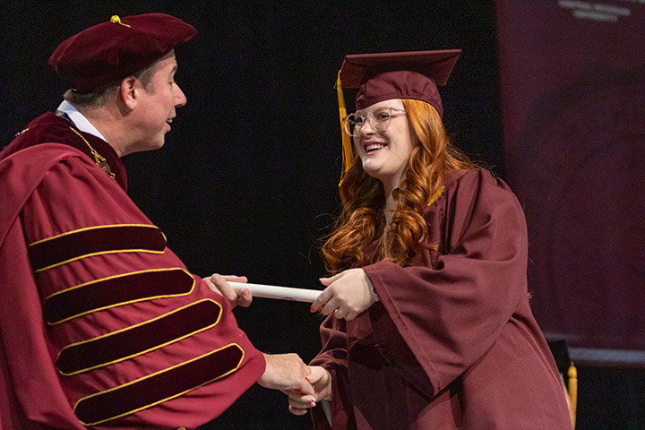 A man and woman in graduation caps and gowns shaking hands.
