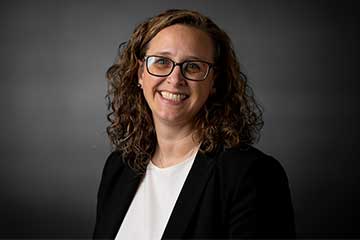 A smiling woman with blond curly hair wearing a white shirt and black blazer