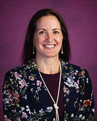 A dark haired woman in a floral jacket in front of a maroon backdrop