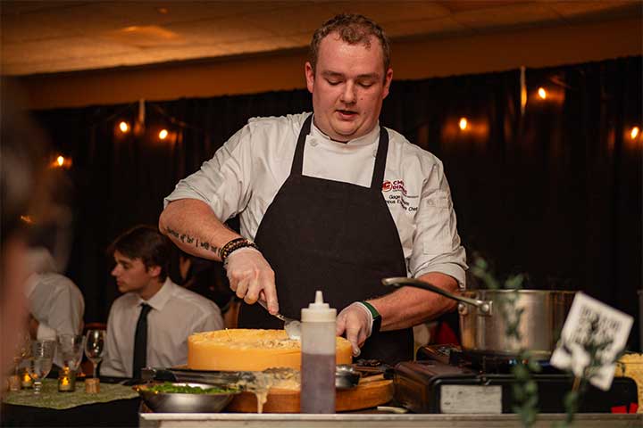 A chef in a white uniform and black apron prepares food at a tableside station