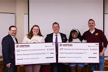 Two female students hold giant checks at an awards presentation