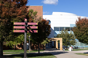 A signpost with arrows pointing in many directions in front of a white building.