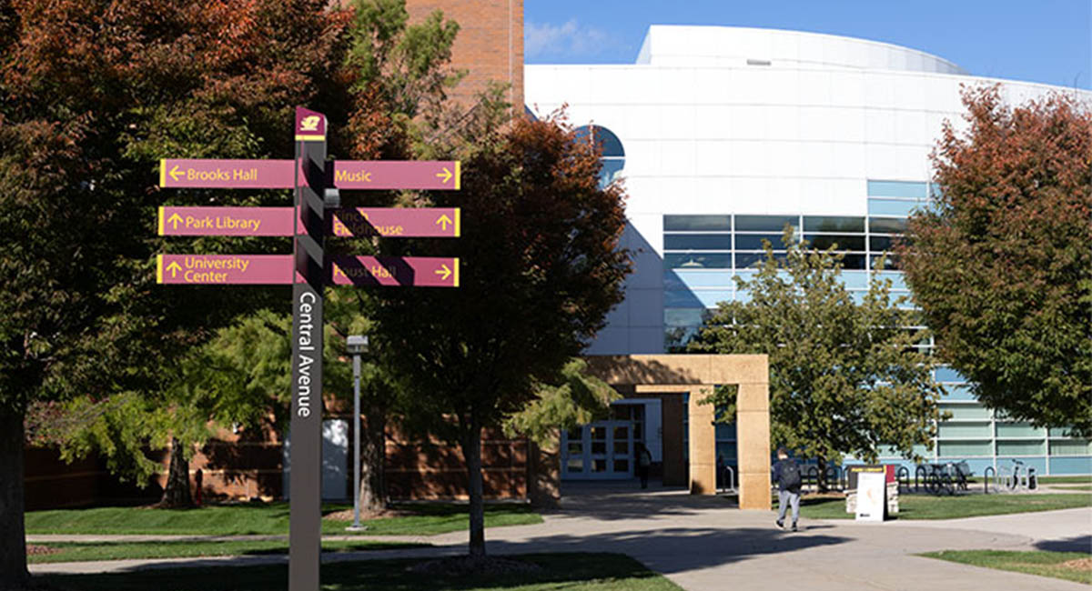 A signpost with arrows pointing in many directions in front of a white building.