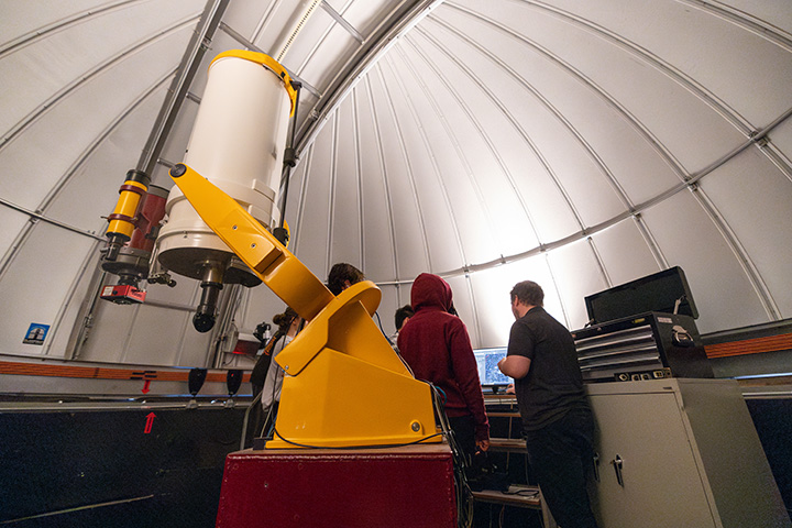 A group of people standing next to a telescope in a dome.