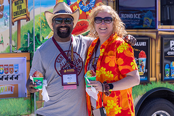 A man in a hand and woman in an orange Hawaiian shirt posing for a picture.