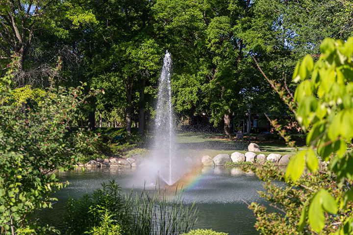 A water fountain in a pond with a rainbow reflecting through the falling water.