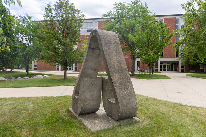 A concrete statue in the shape of an upside down heart stands in a courtyard.