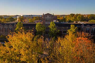 A drone photo of CMU's Warriner Hall surrounded by fall trees on a sunny day