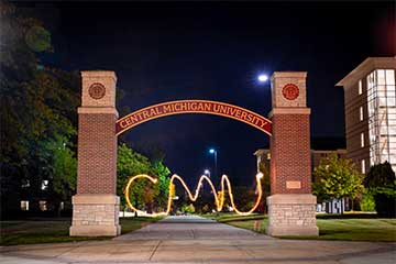 The letters CMU appear in light under an archway at night